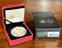 Coin in capsule nestled in red presentation case next to outer box showing label