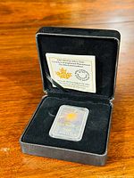 Open black presentation case showing silver coin in plastic capsule and certificate card in lid