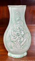 Front view of flattened ovoid celadon porcelain vase with molded lotus motif displayed against wood background.