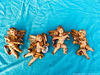 All four cherub figurines laid out on blue fabric background, showing the entire set.