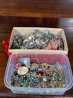 Multiple containers filled with a variety of estate jewelry including necklaces, bracelets, earrings, brooches, pins, and other decorative pieces in different materials and colors.