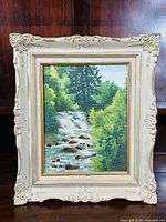 Photo of the full framed oil on board painting showing the waterfall and lush foliage scene with decorative frame.