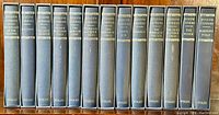 Front view of all 13 books in navy blue slipcases showing titles and author name on spines.