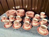 Full set displayed on table showing cups, saucers, plates and bowls in red and white Staffordshire transferware pattern.