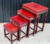 Set of 4 red-brown carved rosewood nesting tables displayed nested side view showing size progression and intricate carvings on aprons and legs.