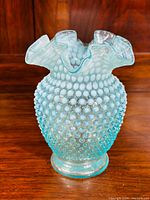 Front view of blue hobnail opalescent vase on wooden surface.