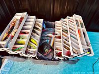 Wide angle photo showing the full opened tackle box with multiple compartments filled with various vintage fishing lures and tackle items