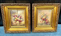 Pair of two square vintage ornate gold gilded frames featuring floral prints under glass set on blue fabric.