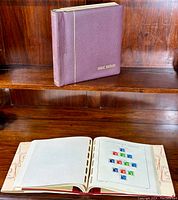Closed purple hardcover binder with gold 'GREAT BRITAIN' text, next to open binder showing stamp album pages with mounted stamps.