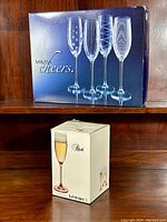 Photo of boxed Mikasa Cheers crystal champagne flutes and boxed Luminarc Rosé champagne flutes on wooden shelf