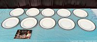 Eleven dinner plates arranged in two rows on turquoise cloth with catalog brochure at front left