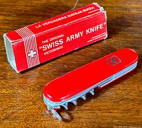 Red Victorinox Swiss Army knife with multiple tools extended, displayed alongside original box showing moderate wear and cut off flaps.