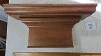 Top-down view showing stepped molding and rectangular wood shelf with a ruler for size reference.