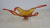 Front view of the art glass centerpiece bowl showing the amber color with red tips and three clear glass supports.