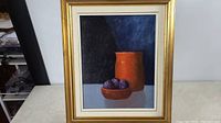 Full view of the framed oil painting showing orange pottery and plums