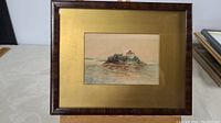 Framed early watercolour painting depicting Boldt Castle on a small island surrounded by water. Painting measures 5.5 by 3.75 inches within a gold-colored mat and a wooden frame.