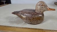 Side view of a wooden carved duck decoy showing detailed feather painting and carved tail structure, placed on table with measuring scale indicating approximate size.