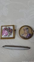 All three items arranged on white textured fabric background: two Limoges brooches and one tie clip.