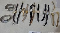 All 11 watches laid out flat on fabric surface showing various band styles and watch faces.