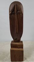 Front view of the entire cedar wood carving showing the elongated stylized human face and the rectangular base.