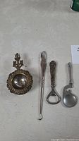 Full set of four items shown together on table: tea strainer, lace puller, bottle opener, tasting spoon