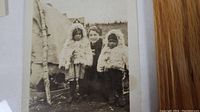 Photo of two children in fur coats flanking a woman outside a tipi, winter clothing visible, vintage sepia tone