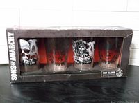 Box containing four Sons of Anarchy pint glasses with varying designs showing skulls and reaper graphics