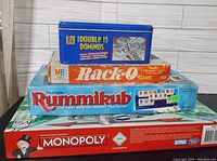 Photo showing stacked boxes of Monopoly, Rack-O, Double 15 Dominos, and Rummikub games.