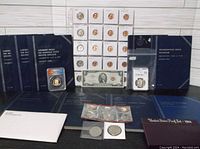 Wide shot showing total lot including coin books, graded coins, carded uncirculated coins in sleeves, sets, and collectible currency bill.