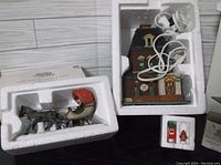 Opened Haberdashery building in styrofoam packaging with wiring for lighted feature, and One Horse Open Sleigh in separate styrofoam insert with horse and sleigh visible.