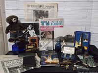 Photo showing complete lot with magazines, figurines, blue glass bottles, cufflinks, tie clips, and other collectible items arranged on table.