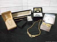 Full view of jewelry items including gold-tone necklace in open box, multiple earrings, rings, collectible plate and pin boxes arranged on white background.
