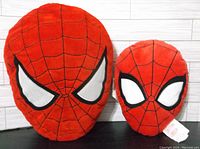 Two Spiderman pillows, one larger and one smaller, showing front with red fabric, black webbing, and white eyes.