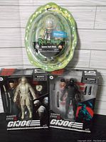 Three boxed action figures. Top: Rick and Morty Space Suit Rick. Bottom left: Storm Shadow #17 GI Joe figure. Bottom right: Snake Eyes #16 GI Joe figure.