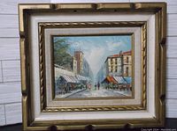 Framed oil painting on board showing a European street market scene with buildings, stalls, and pedestrians, sized about 16 x 15 x 2 inches.