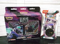 New sealed Shadow Rider Calyrex VMAX League Battle Deck box alongside the Scarlet & Violet Obsidian Flames booster pack and coin in original packaging