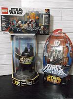 Photo showing all three items together: LEGO set 75310 box on top, Darth Vader figure in cylindrical plastic display to the left, and General Grievous figure in blister packaging to the right.