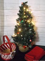Artificial tabletop Christmas tree decorated with lights and burlap base.