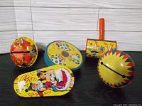 Front view of all five vintage litho tin noise makers showing colorful designs and wood handles