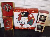 Photo showing Fitz and Floyd Merry & Bright snowman box, Lenox Santa Claus wall decorations, and Hallmark red pine cone ornaments with boxes
