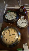 Photo showing four clocks arranged on a surface: large decorative wall clock, two round wall clocks, and one small wooden mantle clock.