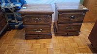 Front view of two brown wooden bedside tables with carved floral details on top drawers, metal handles, visible scratches.
