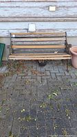Front view of weathered wooden outdoor bench with iron side armrests and backrest showing slats and condition.