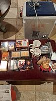 Photo showing multiple stacks of collector trading cards, two coffee mugs, assorted pins in small boxes, and a ceramic cowboy bust figure.