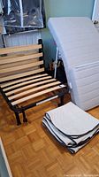 IKEA Lycksele chair bed frame with mattress standing vertically and folded cushion covers on floor nearby.