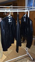 Three black leather jackets hanging on white clothing rack, showing the overall look and condition.