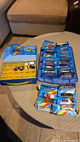Overview photo showing a collection of Matchbox cars in their original blue boxes arranged in rows, with a blue and yellow plastic Matchbox carry case containing three loose cars next to them.