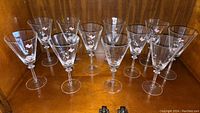 Ten Mikasa crystal glasses with etched butterfly patterns, displayed in a wooden cabinet.