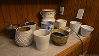 View showing 11 ceramic planting pots of various sizes and designs against a wooden wall, including textured and painted designs ranging from 4 to 10 inches.