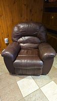 Front view of over-stuffed dark brown pleather recliner chair showing padded backrest, seat, and armrests.